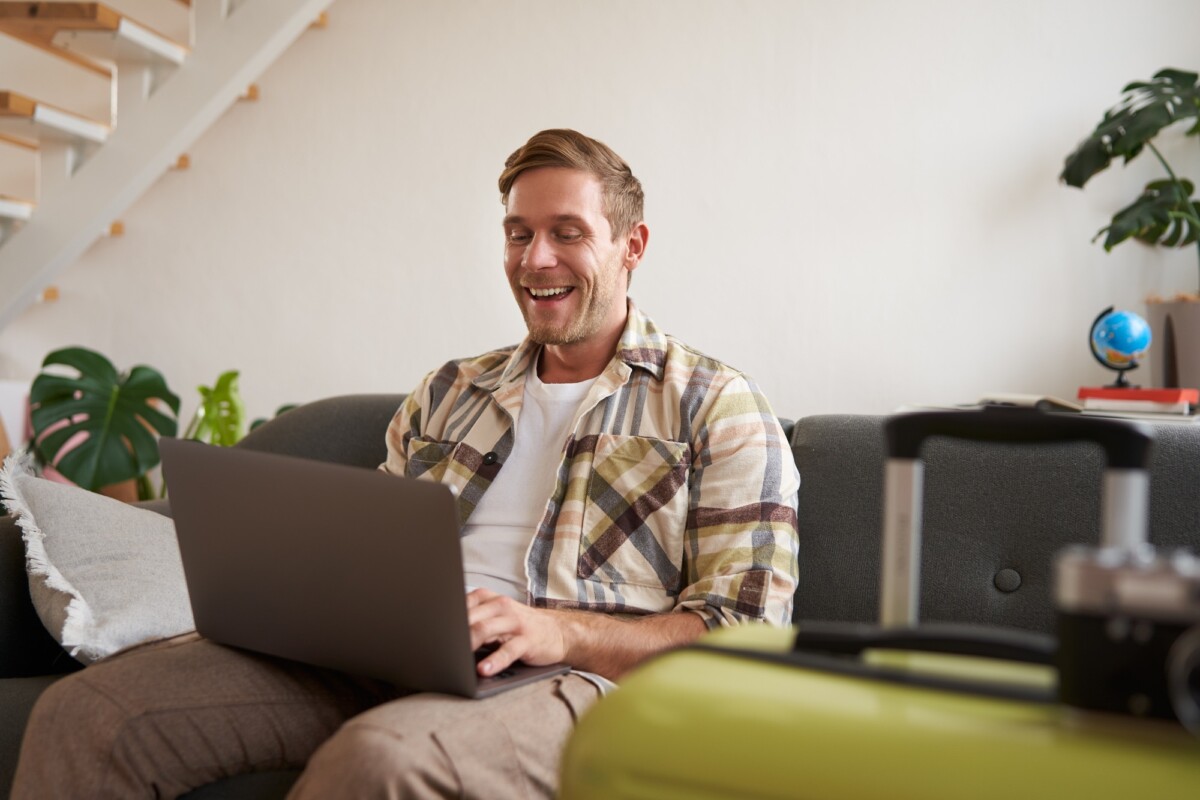 Portrait of happy young man, tourist booking his holiday with travel agency, looking at laptop Portrait of happy young man, tourist booking his holiday with travel agency, looking at laptop